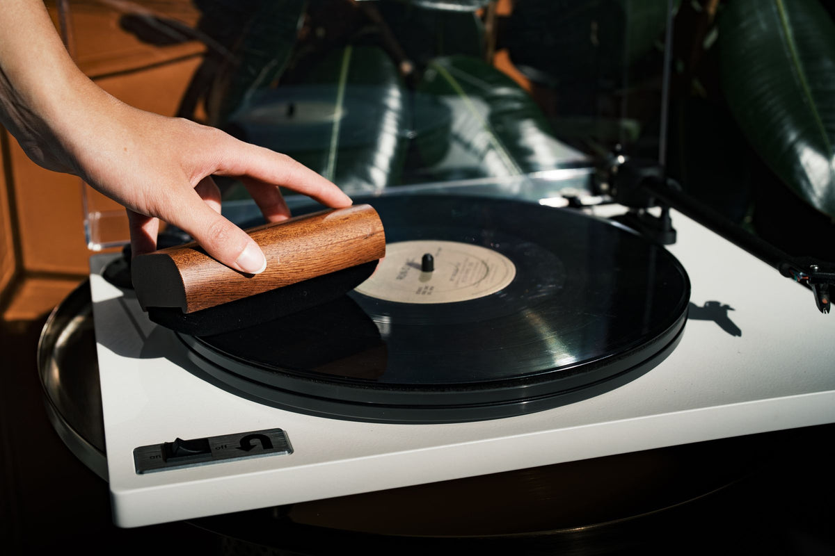 A velvet brush cleaning a record on a white turntable